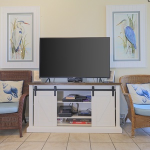 A cozy seating area features two chairs with blue cushions, a TV on a stylish cabinet, and beach-themed artwork