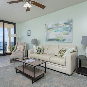 Living area features a light sofa with queen sleeper, a modern coffee table, and stunning views of the beach from the balcony