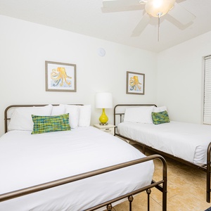 Rest in this guest bedroom featuring two comfortable queen beds, colorful decor, and natural light from the window
