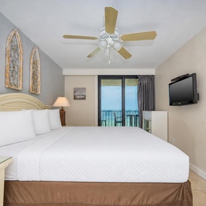 The master bedroom features a comfortable king bed, stylish decor, a flat-screen TV, and a lovely view from the balcony