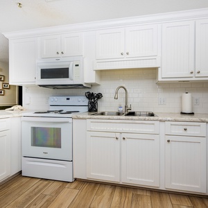 Prepare meals in the bright kitchen featuring white cabinetry, granite countertops, and white appliances