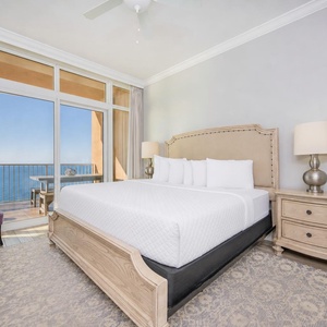 Relax in the master suite featuring a plush king bed, elegant decor, and stunning beach views from the balcony