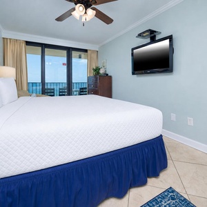 The master bedroom features a king bed, a flat-screen TV, and a lovely view of the balcony overlooking the beach