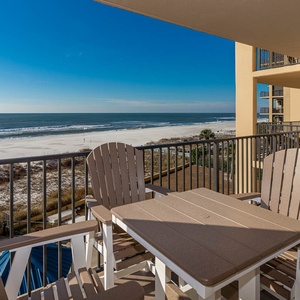 A cozy balcony features comfortable seating and a table, offering a serene view of the beach and tranquil blue waters