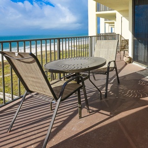 Balcony seating with a round table overlooks the beach, providing a perfect spot to relax and enjoy the gulf view