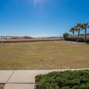 Lush green grass leads to a serene view of the beach, framed by palm trees under a clear blue sky