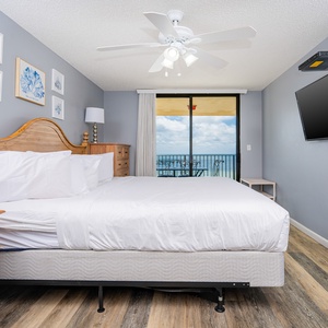 Bright master bedroom featuring a wooden king bed, modern decor, and a balcony with a view of the beach and outdoor seating