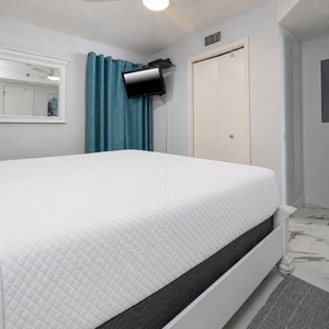 A cozy bedroom features a plush king bed, teal curtains, a mounted TV, and elegant marble flooring, creating a serene retreat