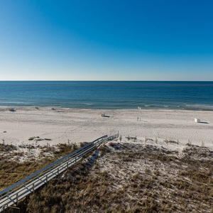 A serene view of the beach front reveals soft white sand and gentle waves under a clear blue sky