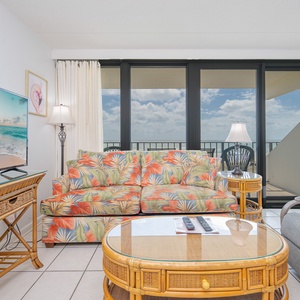 Inviting coastal living space features a tropical-patterned sofa, large TV, and stunning views through expansive windows