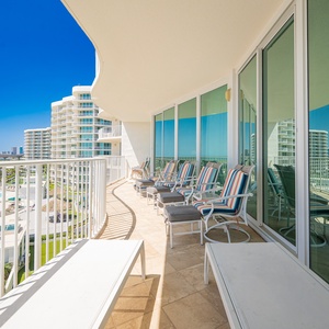 Relax on the spacious balcony with colorful loungers, enjoying expansive views of the shimmering pool and vibrant blue sky