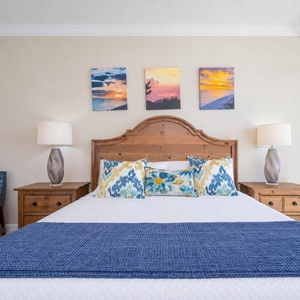 The king bed in the master suite invites restful sleep under warm bedside lamp glow and coastal art above