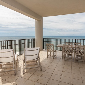 This expansive balcony features comfortable seating and a dining table, perfect for enjoying panoramic beachfront views