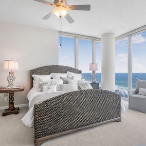 The master bedroom features a plush bed with decorative pillows and a stunning beach view through large windows