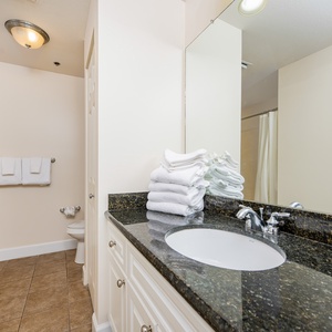 The master bath features a sleek granite countertop, ample white towels, and a relaxing tub-shower for a rejuvenating stay