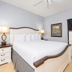 A serene bedroom features a plush king bed, elegant white furniture, and a cozy ambiance enhanced by a bedside lamp