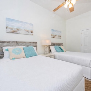 Guest bedroom featuring two double beds with coastal decor, a bedside lamp, and beach-inspired artwork on the walls