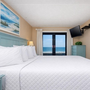 The master bedroom features a plush king bed and a stunning beachfront view through sliding glass doors
