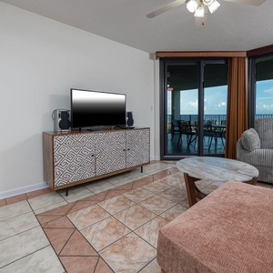Living area features a plush sofa, sleek TV, and a view of the extended balcony overlooking the beach, perfect for relaxation