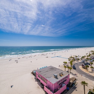 Sunlight sparkles on the coastline as you watch lively beachgoers from your balcony