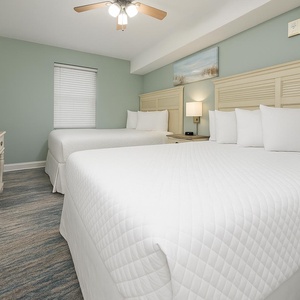 Two comfortable queen beds with crisp white linens and a mounted TV create a serene atmosphere in this inviting guest room