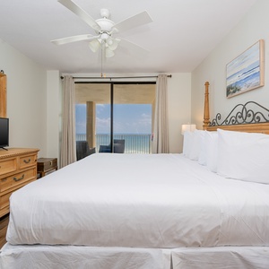 The master bedroom features a king-sized bed, a TV, and a stunning beachfront view from the large sliding glass doors
