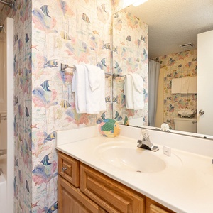 Guest bathroom features a tub/shower combo, wooden cabinetry, and playful fish-themed accents