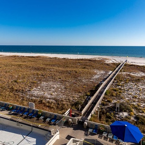 Expansive view of the beach from the balcony, with a winding path leading to the shore and lounge chairs in the pool area