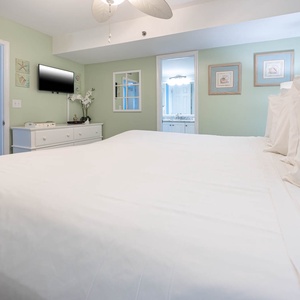 Relax in this serene bedroom featuring an inviting king bed, soft green walls, and a flat-screen TV for your entertainment