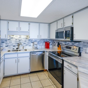 Kitchen featuring sleek cabinetry, a marbled countertop, and a breakfast bar with a Keurig, coffee maker, and red accents