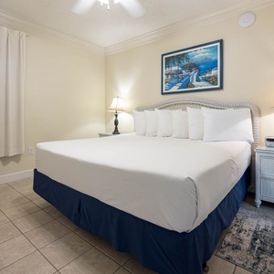 The bedroom features a plush king bed, bedside lamps, and a vibrant coastal painting above the headboard