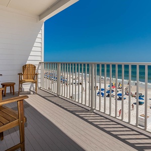 This inviting balcony features wooden chairs and a stunning view of the beach, perfect for relaxing and enjoying the scenery