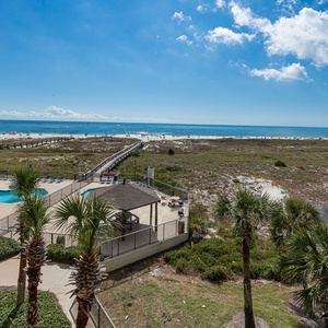 Stunning view of the beach and gulf from the balcony, featuring a pool area surrounded by lush greenery and palm trees