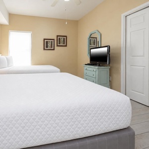This guest bedroom features two comfortable full beds, a flat-screen TV, and soft yellow walls for a cheerful ambiance