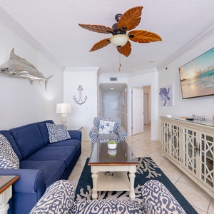 Cozy living area features a navy sofa with decorative pillows, patterned chairs, and a large TV, perfect for relaxation