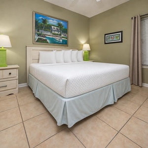The bedroom features a king bed with plush pillows, a vibrant green lamp, and tropical artwork on the walls