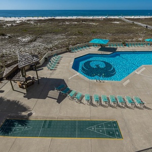 Inviting pool area features a sparkling blue pool, lounge chairs, and a shuffleboard court, all with a view of the beach