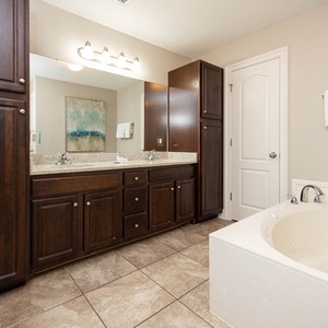 The master bath features dark wood cabinetry, a relaxing jetted tub, and a spacious vanity with dual sinks