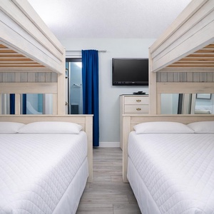 This guest bedroom features two cozy bunk beds, a mounted TV, and a bright atmosphere with a view