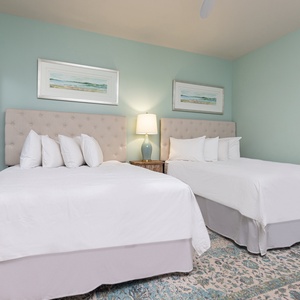 This guest bedroom features two comfortable beds, soft white linens, and serene aqua walls, creating a restful retreat