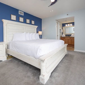 The master bedroom features a king bed with plush pillows, a stylish lamp, and a view into an adjoining bathroom