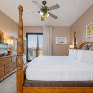 Relax in the spacious master bedroom featuring a four-poster king bed, dresser, and a view through large windows