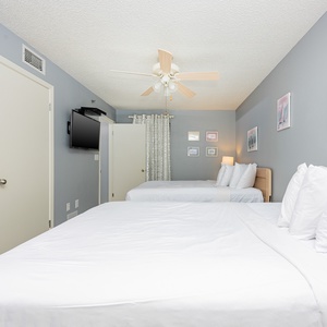 Guest bedroom featuring two queen beds with crisp white linens, a flat-screen TV, and soft coastal artwork on the walls