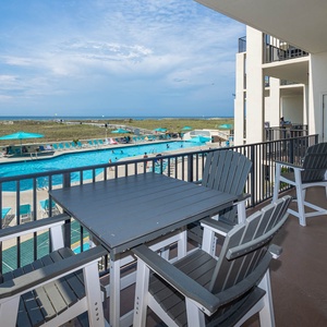The balcony overlooks the sparkling pool area and the beach, creating a perfect spot to relax and enjoy the view