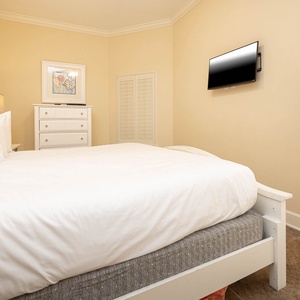 This cozy bedroom features a plush king bed, a mounted TV, and soft beige walls, creating a relaxing retreat for guests