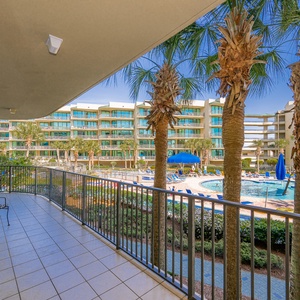 Savor the warm breeze on the balcony, surrounded by lush palms and the vibrant pool scene below