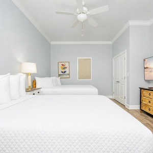 Inviting guest bedroom featuring two queen beds, a large TV, and soft coastal decor for a restful stay