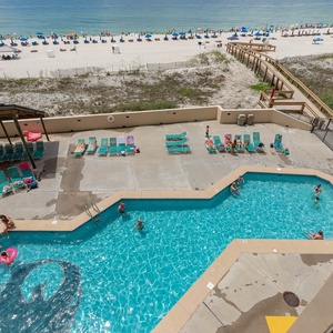 This vibrant pool area features a sparkling blue pool surrounded by lounge chairs and a scenic view of the beach