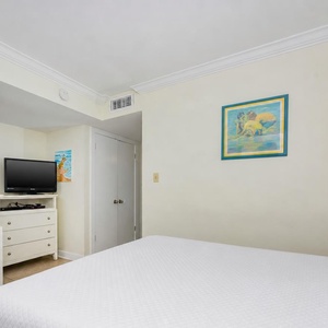 The bedroom features a comfortable bed, a TV for entertainment, and cheerful artwork, perfect for relaxation
