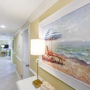 Brightly colored artwork of a beach scene complements the inviting hallway leading to the living area with a TV and seating